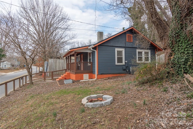 rear view of house with covered porch, an outdoor fire pit, a chimney, and fence