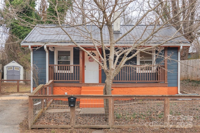 view of front of home with metal roof, a fenced front yard, a storage shed, and a porch