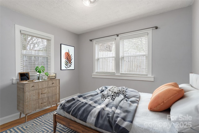 bedroom with multiple windows, a textured ceiling, baseboards, and wood finished floors