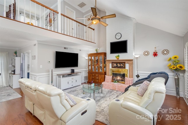 living room featuring high vaulted ceiling, a fireplace, hardwood / wood-style flooring, ceiling fan, and crown molding