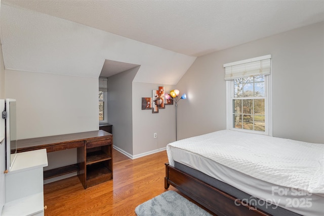 bedroom with lofted ceiling, light hardwood / wood-style flooring, and a textured ceiling