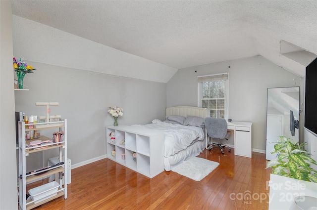 bedroom with wood-type flooring, vaulted ceiling, and a textured ceiling