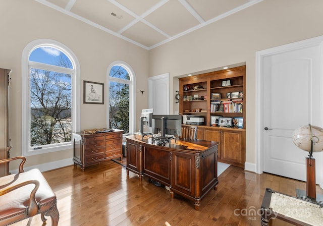 office space with wood-type flooring, coffered ceiling, and a high ceiling