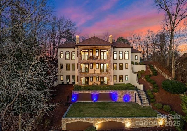 back house at dusk with a balcony and a yard