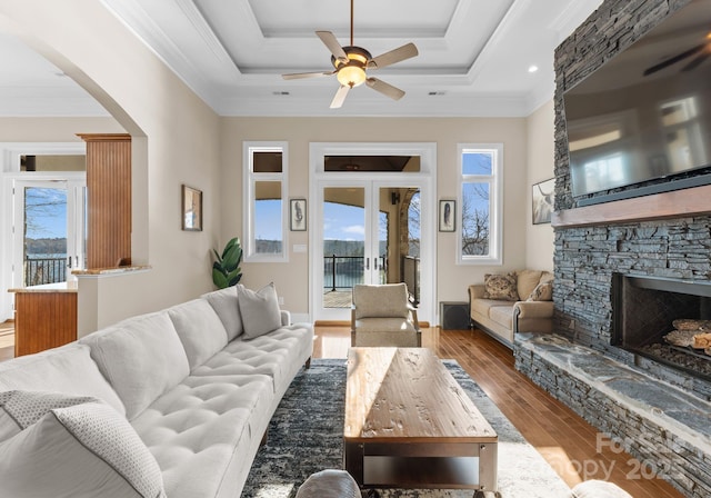 living room featuring crown molding, wood finished floors, a stone fireplace, arched walkways, and ceiling fan