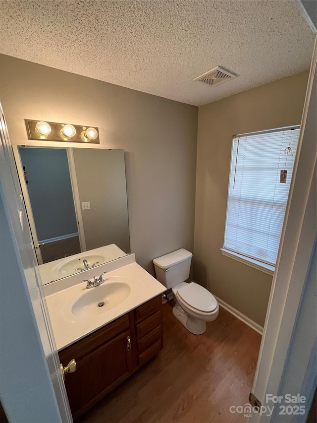 bathroom featuring wood-type flooring, toilet, vanity, and a textured ceiling