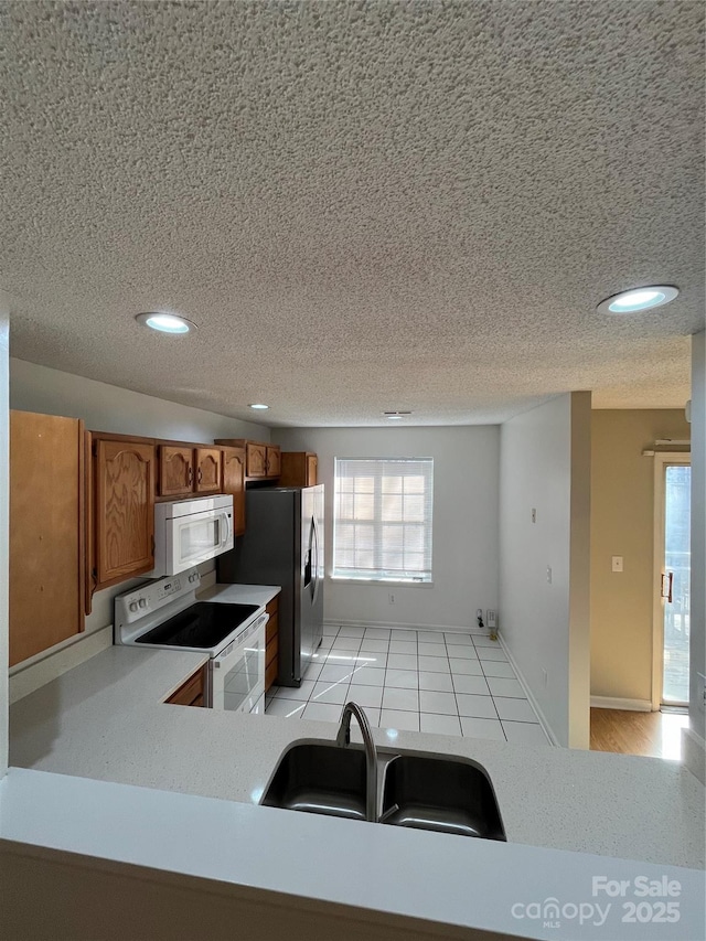 kitchen featuring sink, white appliances, light tile patterned floors, and a textured ceiling