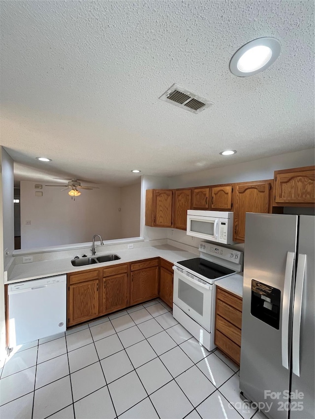 kitchen featuring sink, white appliances, light tile patterned floors, and a textured ceiling