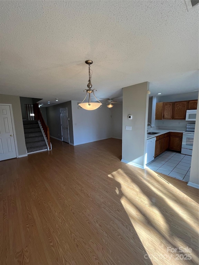 unfurnished living room featuring ceiling fan, sink, a textured ceiling, and light hardwood / wood-style floors