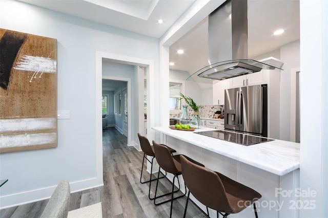 kitchen featuring stainless steel fridge, a breakfast bar area, white cabinetry, island range hood, and kitchen peninsula