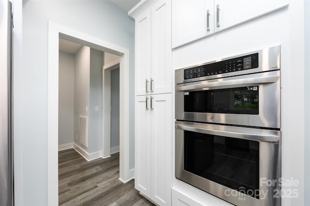 kitchen with white cabinetry, stainless steel double oven, and dark wood-type flooring