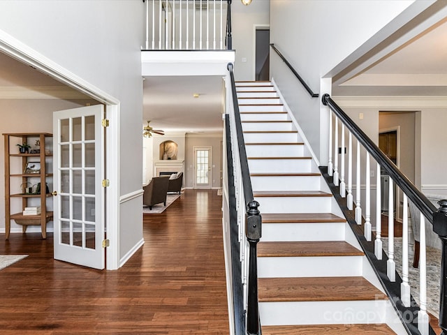 stairs with crown molding, a fireplace, a towering ceiling, and wood finished floors