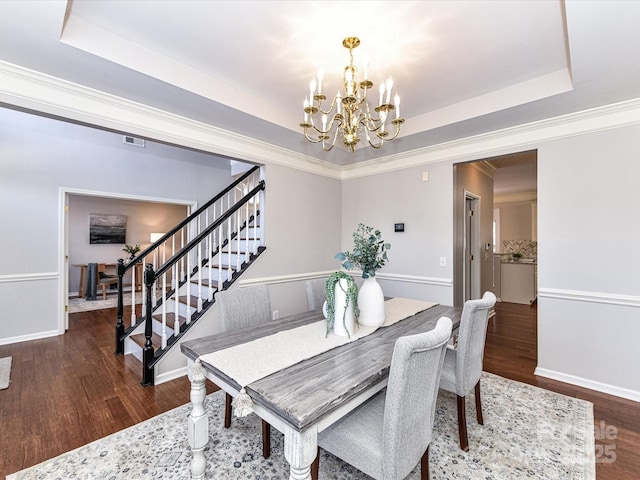 dining area featuring a raised ceiling, stairway, dark wood-style flooring, and an inviting chandelier