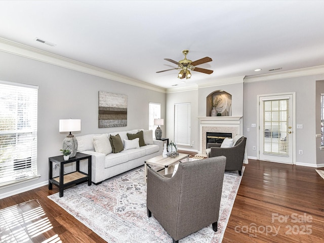 living room featuring dark wood-style flooring, a glass covered fireplace, visible vents, and baseboards