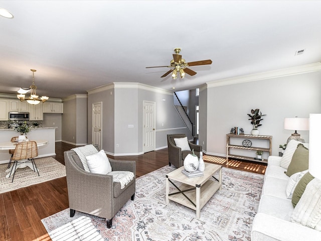 living area with crown molding, light wood finished floors, visible vents, baseboards, and ceiling fan with notable chandelier