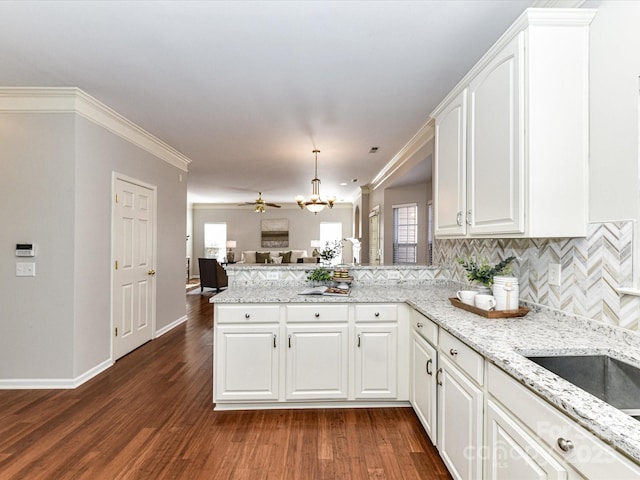 kitchen featuring dark wood-style flooring, decorative light fixtures, crown molding, white cabinets, and a peninsula