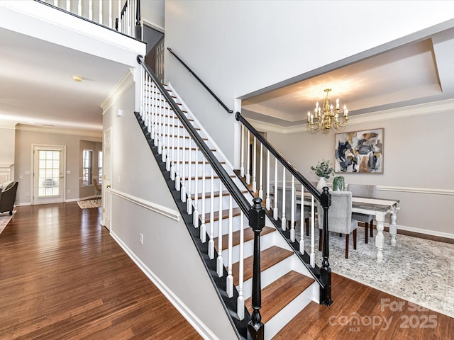 stairway featuring an inviting chandelier, a tray ceiling, wood finished floors, and ornamental molding