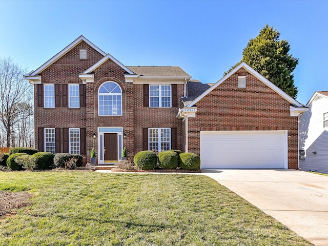 colonial house with a garage, a front yard, concrete driveway, and brick siding