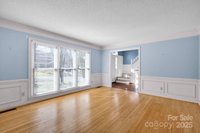 spare room with ornamental molding, a textured ceiling, and light hardwood / wood-style floors