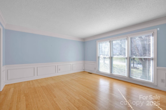 unfurnished room featuring light hardwood / wood-style flooring, ornamental molding, and a textured ceiling