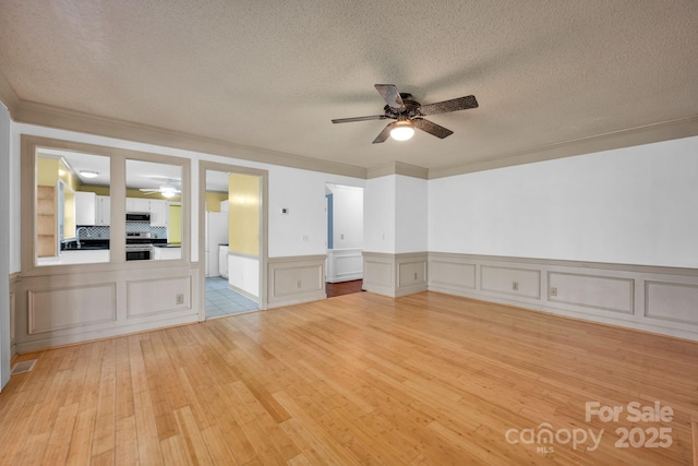 spare room with ceiling fan, ornamental molding, light hardwood / wood-style floors, and a textured ceiling