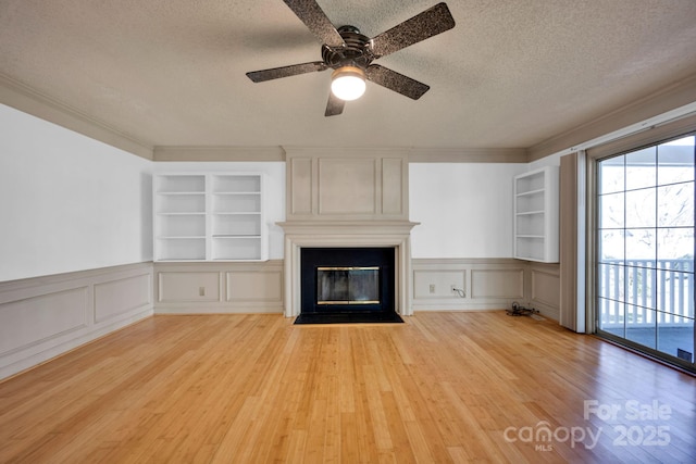 unfurnished living room with crown molding, a fireplace, a textured ceiling, built in shelves, and light wood-type flooring