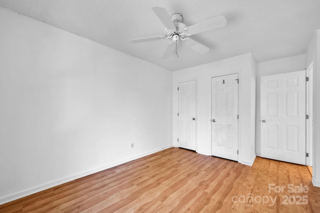 unfurnished bedroom with multiple closets, ceiling fan, light hardwood / wood-style floors, and a textured ceiling