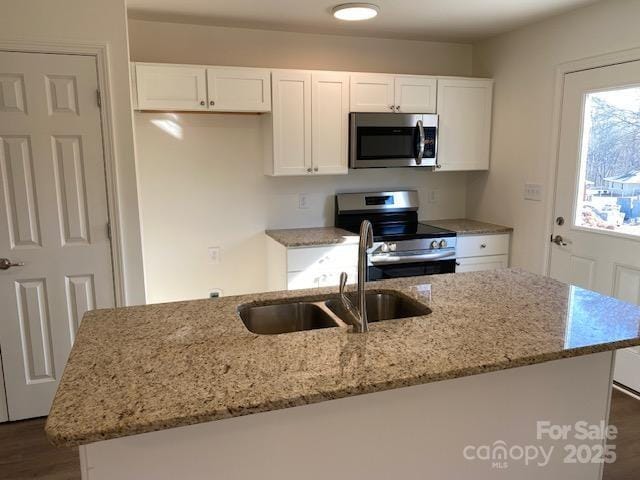 kitchen featuring stainless steel appliances, light stone countertops, a center island with sink, and white cabinets