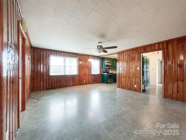 unfurnished living room featuring ceiling fan and wood walls