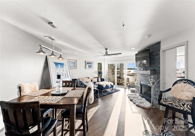 dining area featuring a ceiling fan, visible vents, a fireplace, and wood finished floors