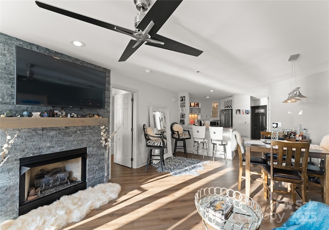 living area featuring a stone fireplace, wood finished floors, a ceiling fan, and recessed lighting