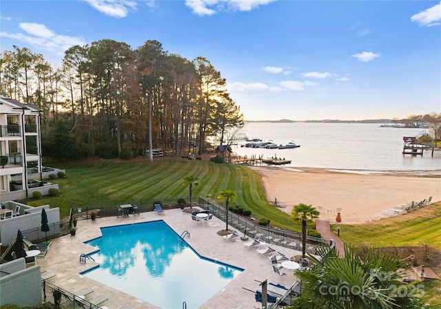 community pool with a lawn, fence, a water view, and a patio area