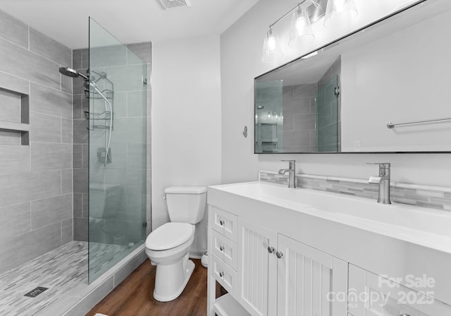 full bath with a tile shower, toilet, visible vents, wood finished floors, and vanity