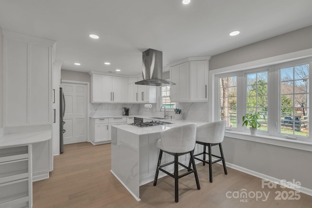 kitchen featuring a breakfast bar, sink, white cabinetry, island range hood, and kitchen peninsula