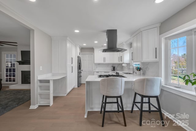 kitchen with tasteful backsplash, white cabinetry, island range hood, and kitchen peninsula