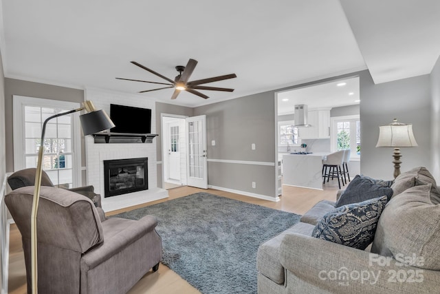 living room with ornamental molding, a fireplace, light hardwood / wood-style floors, and ceiling fan