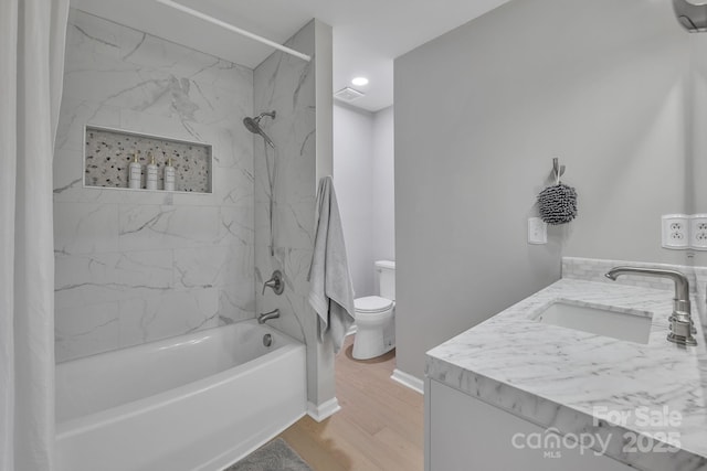 full bathroom with a wall mounted air conditioner, hardwood / wood-style floors, tiled shower / bath combo, vanity, and toilet