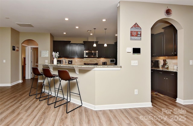 kitchen with light stone countertops, a breakfast bar, light hardwood / wood-style floors, and decorative light fixtures