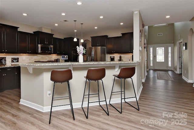 kitchen featuring appliances with stainless steel finishes, pendant lighting, a kitchen bar, a center island, and light hardwood / wood-style floors