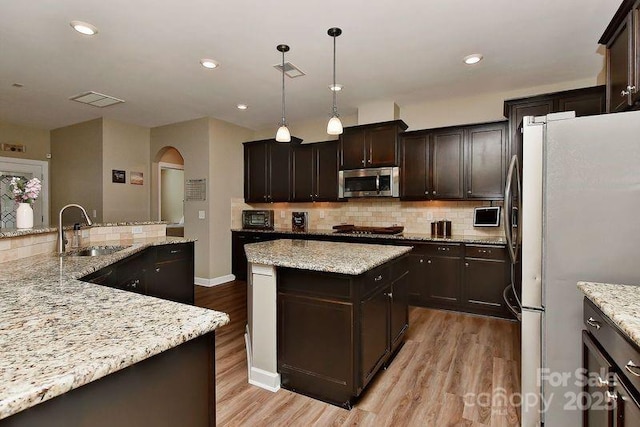 kitchen with a kitchen island, pendant lighting, sink, stainless steel appliances, and light stone countertops