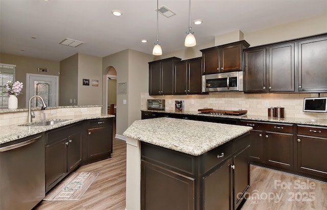 kitchen featuring a kitchen island, sink, hanging light fixtures, stainless steel appliances, and dark brown cabinets