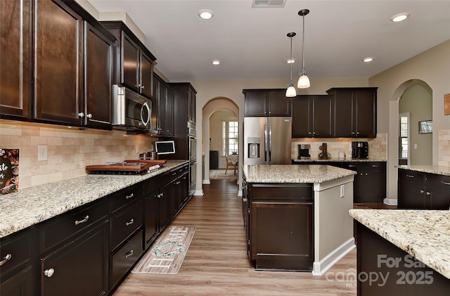 kitchen featuring a center island, dark brown cabinets, hanging light fixtures, light wood-type flooring, and appliances with stainless steel finishes