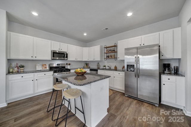 kitchen featuring stainless steel appliances, white cabinetry, dark stone countertops, and dark hardwood / wood-style flooring