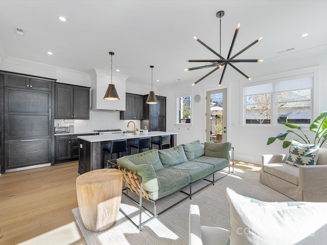 living room with crown molding, a chandelier, sink, and light hardwood / wood-style flooring