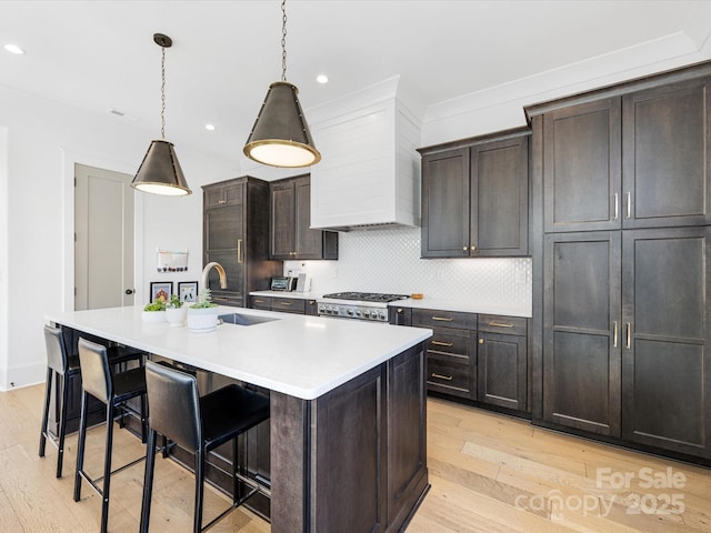 kitchen featuring pendant lighting, sink, a breakfast bar area, a kitchen island with sink, and custom range hood