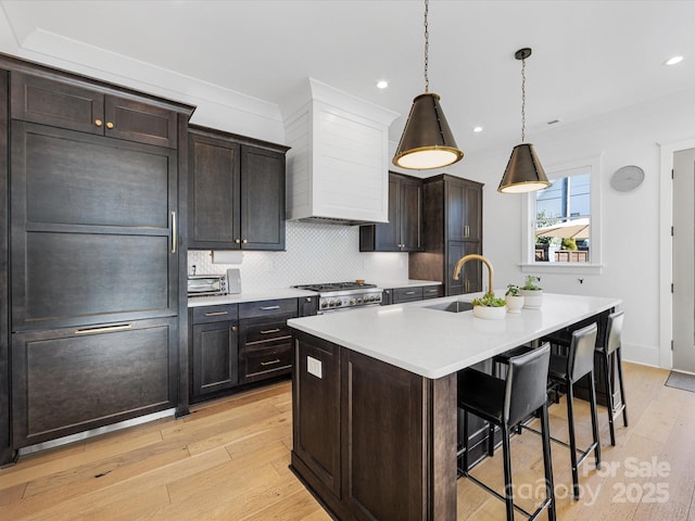 kitchen featuring premium range hood, decorative light fixtures, sink, a breakfast bar area, and a center island with sink