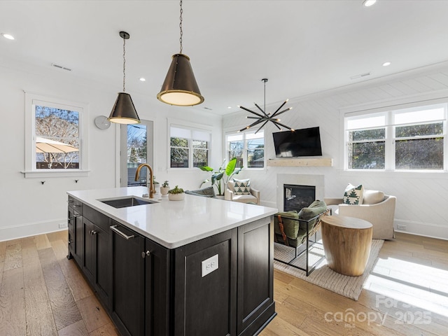 kitchen featuring sink, hanging light fixtures, a kitchen island with sink, crown molding, and light hardwood / wood-style flooring