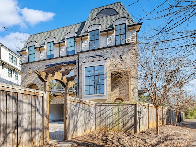french provincial home featuring brick siding, fence, a shingled roof, and mansard roof