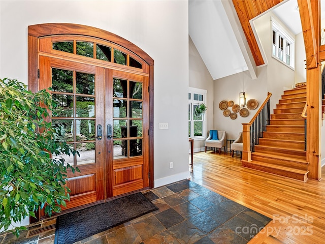 foyer entrance featuring high vaulted ceiling, stone tile floors, baseboards, french doors, and stairway