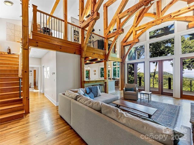 living area featuring french doors, light wood finished floors, a high ceiling, and baseboards